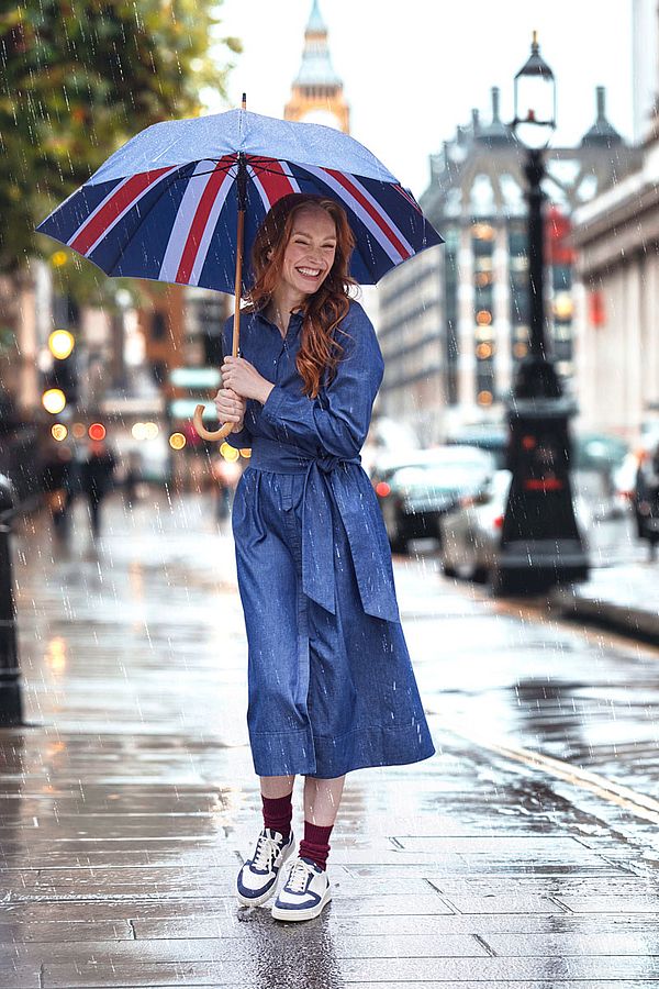 Frau spaziert im Regen mit Regenschirm