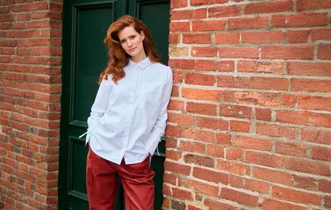 Frau an Haustür in lässiger Bluse und Cordhose