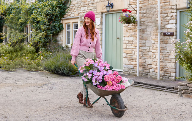 Frau mit roséfarbenen Cardigan mit Schubkarre