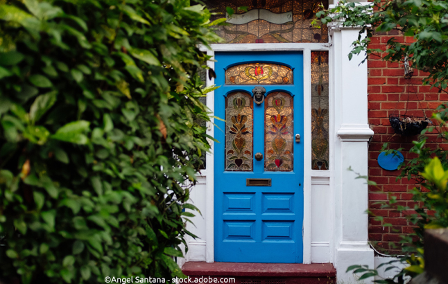 Blaue viktorianische Tür mit Hecke links im Bild